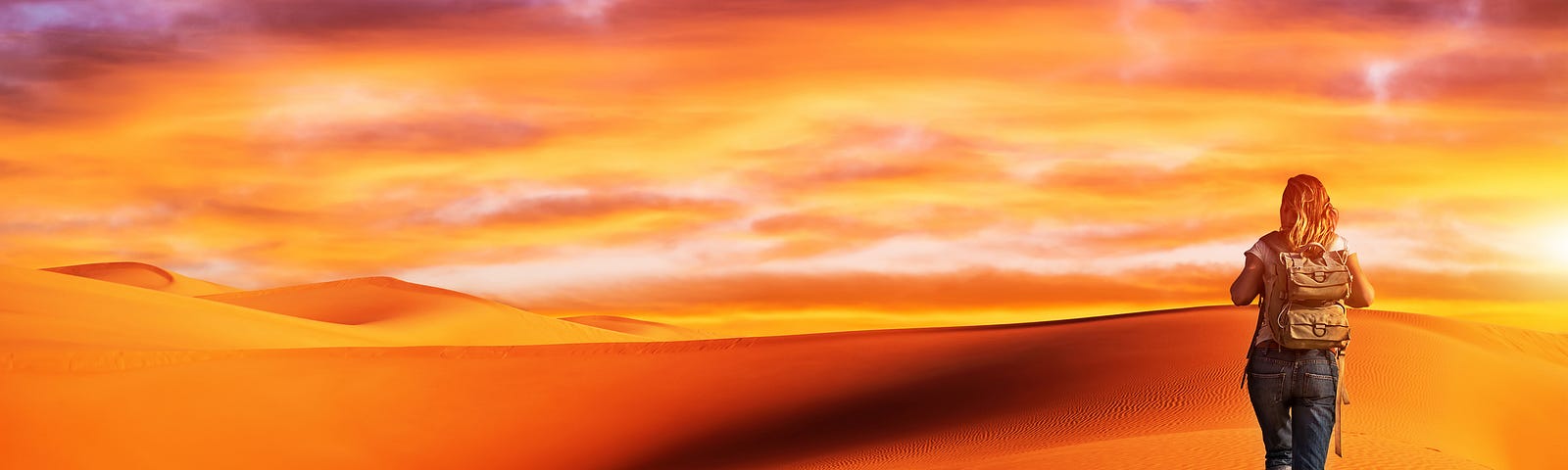 woman hikes across dessert, which is in orange tones with a pink and purple sky