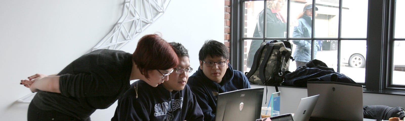 Woman with short red hair leaning over helping two men with laptops.