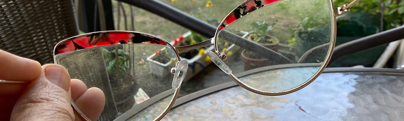 Photo of a woman’s holding out a pair of glasses red/gold glasses at a bistro table, Taken by the poet. Credit, Jane Harris