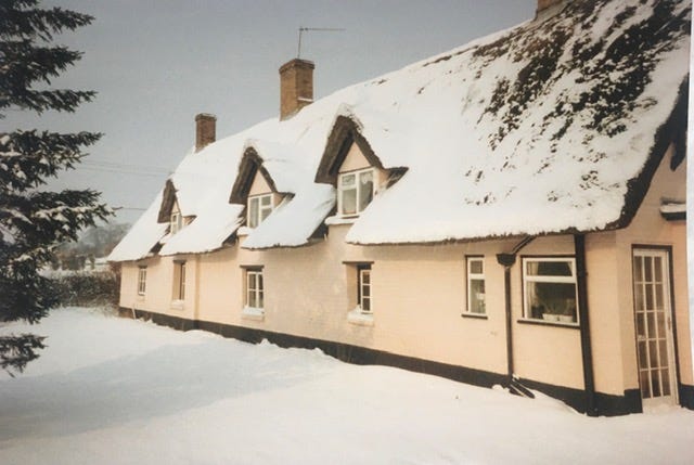Thatched cottage with gable windows, traditional pink exterior, light covering of snow