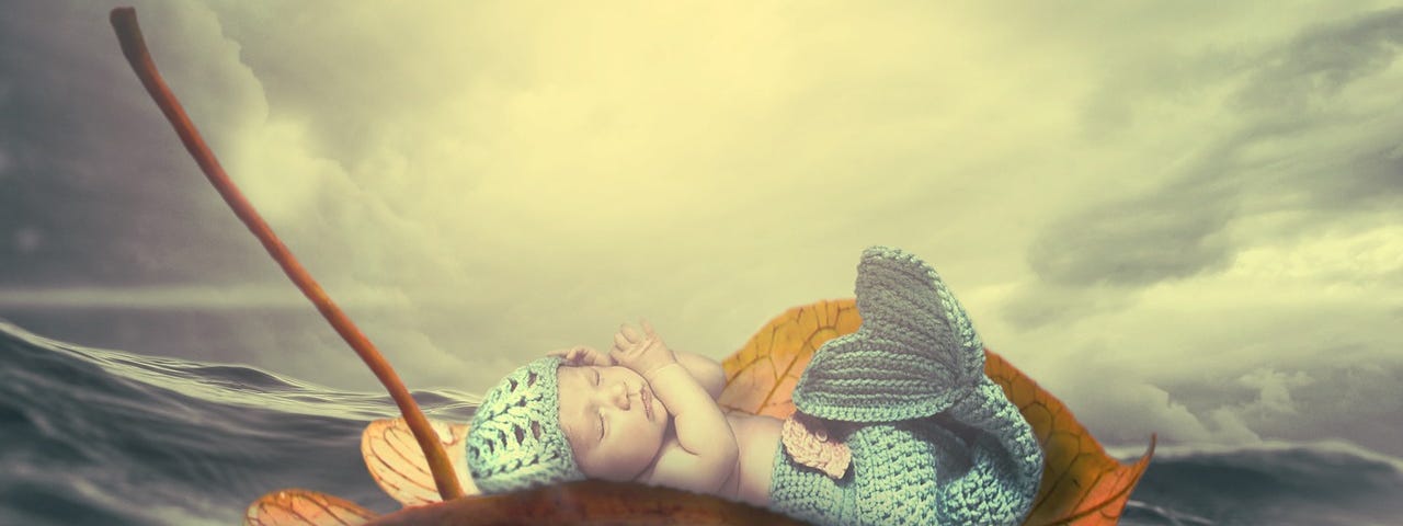 A small baby, wearing a blue crochet mermaid tail and cap, soundly sleeping on a leaf floating on the sea.