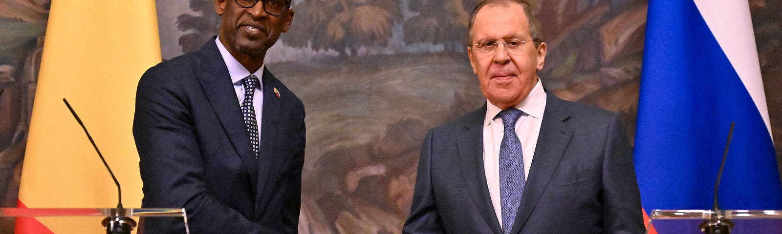 Russian Foreign Minister Sergei Lavrov and his Malian counterpart Abdoulaye Diop shake hands in front of Russian and Malian flags and a large landscape painting.