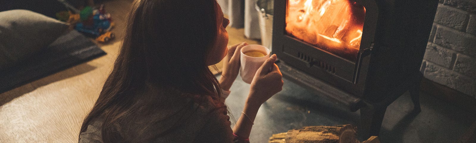 A woman enjoying a warm drink in front of a fireplace.