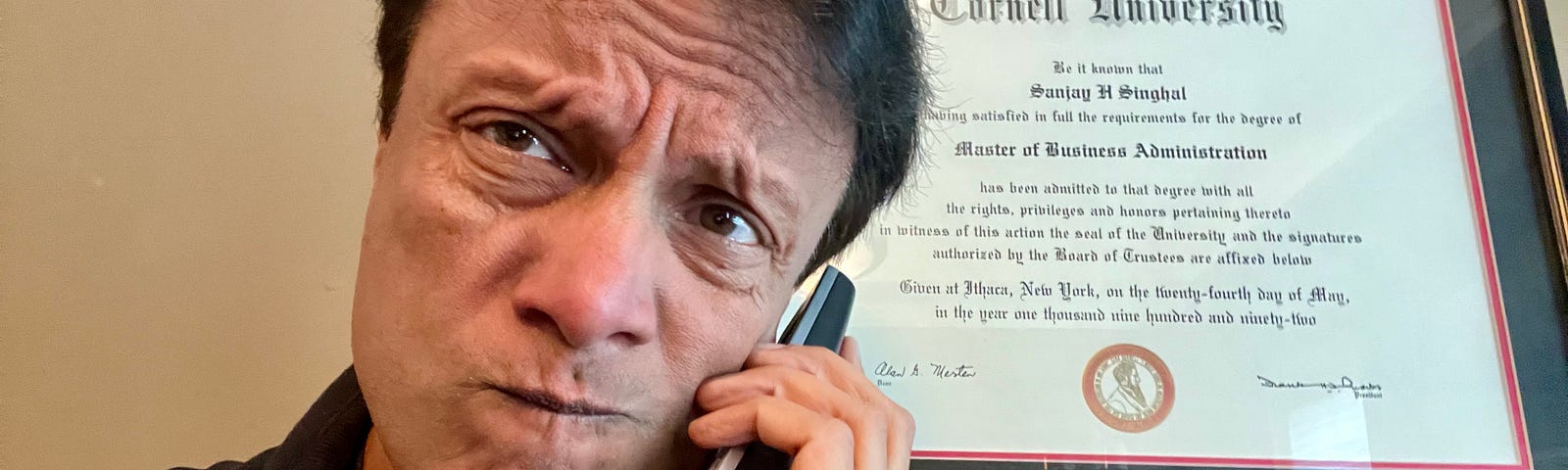 Photo of author on a cordless phone in front of his Cornell MBA diploma