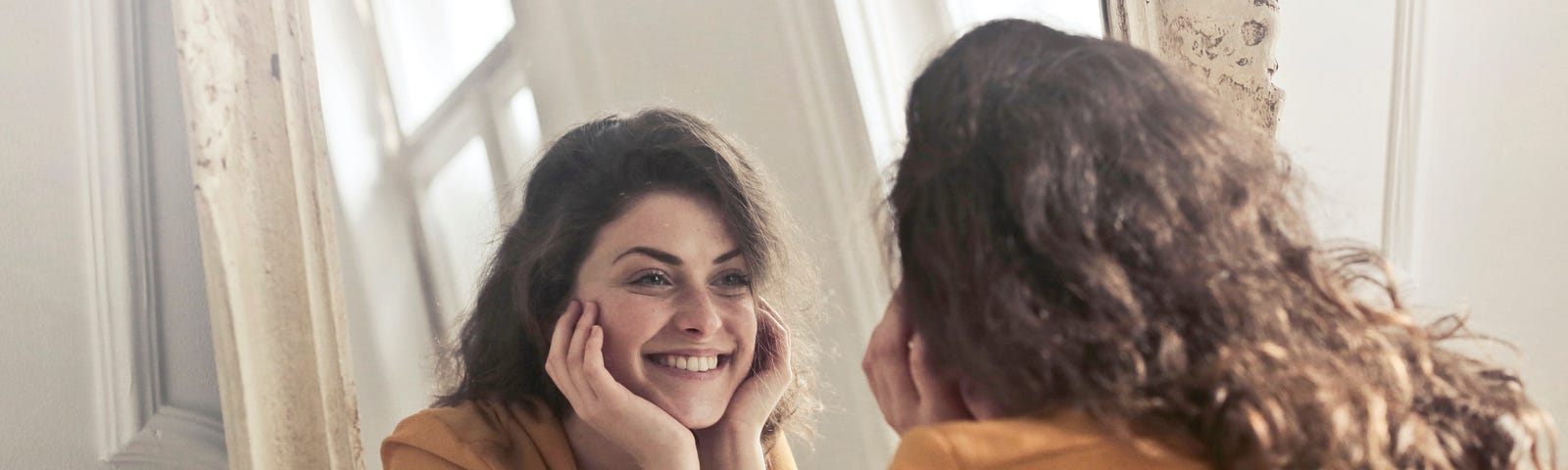 A young lady smiling lovingly at her own reflection in the mirror