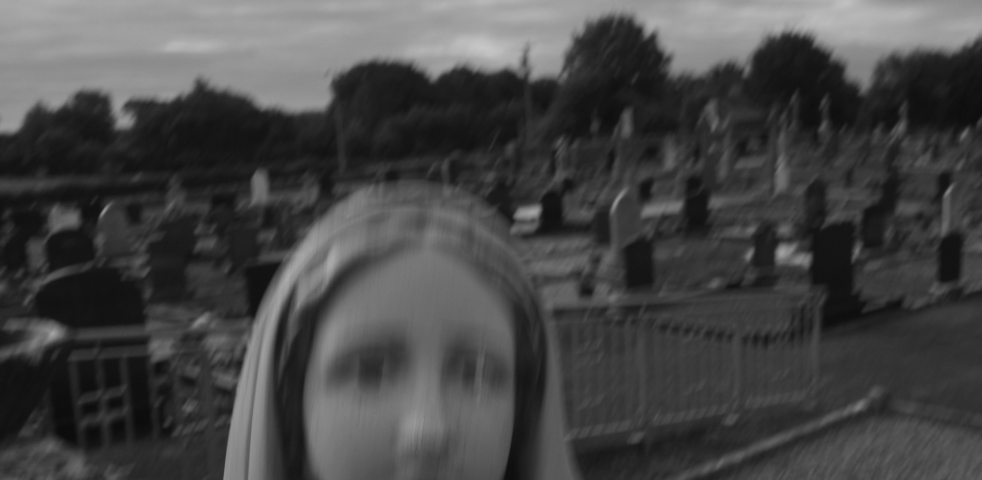 A ghostly figure, against a black-and-white churchyard.