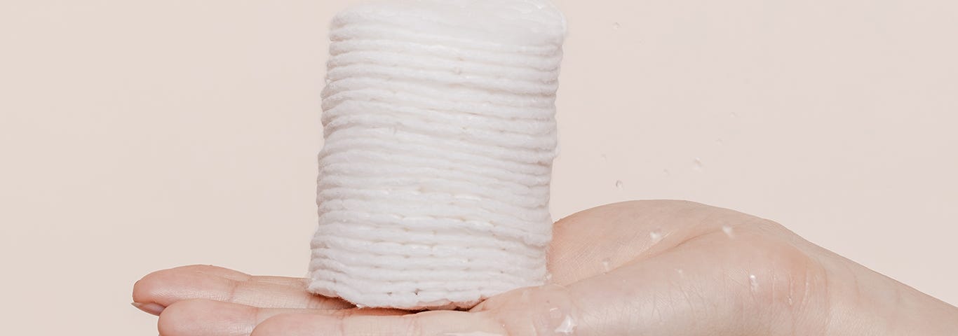 Hand holding a stack of cotton pads to apply toner