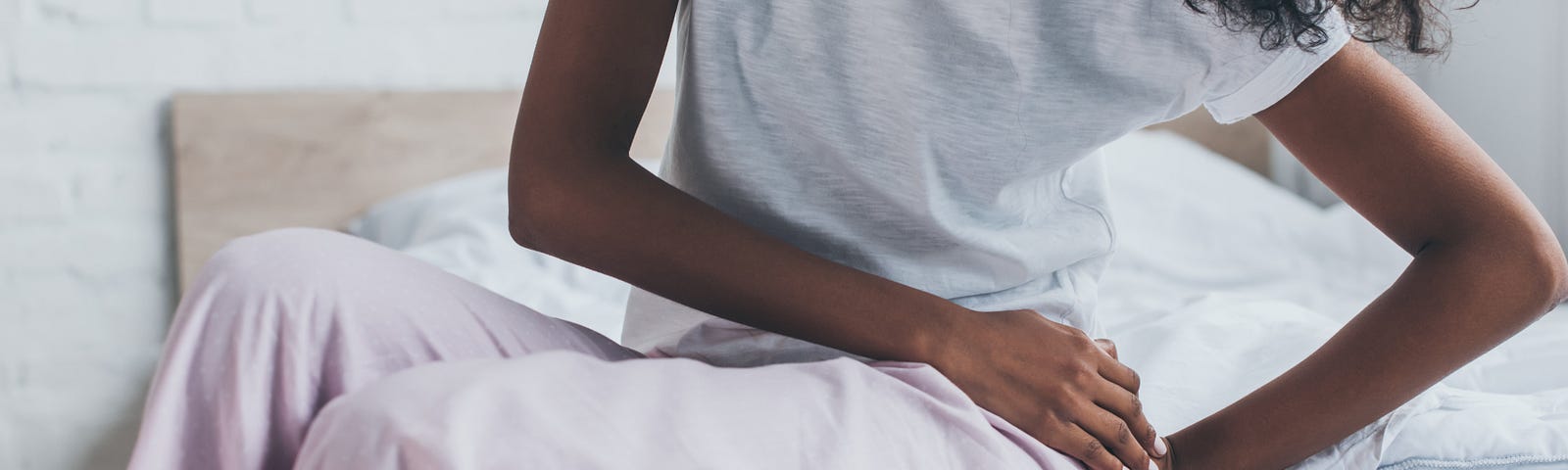 Cropped view of woman suffering from pain in hip while sitting on bed