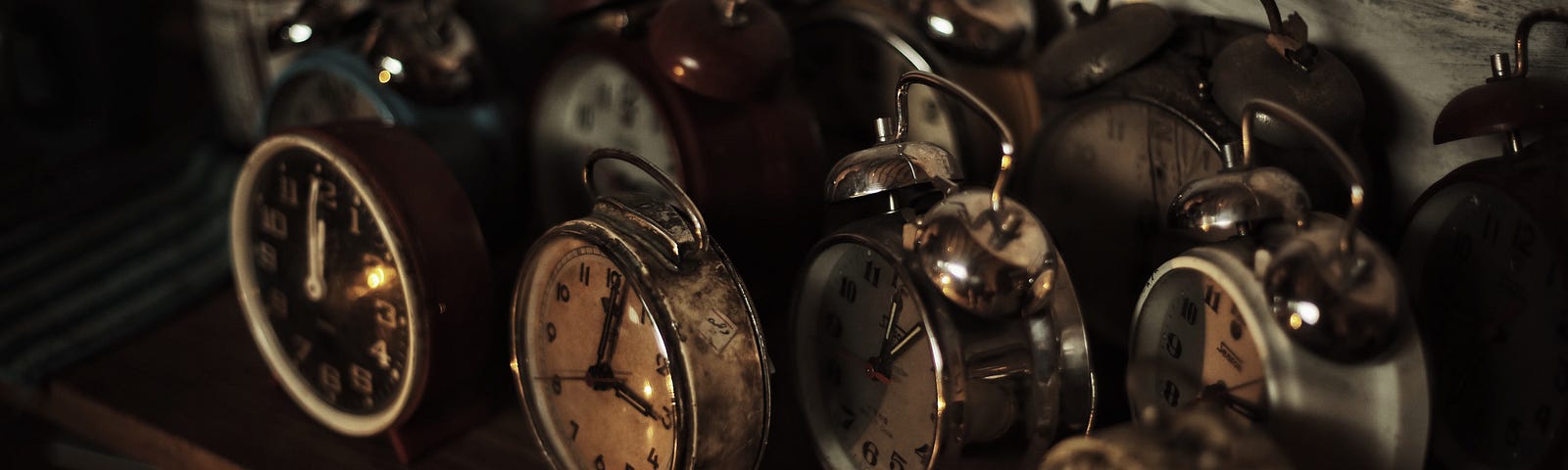 A dark moody photo of a shelf full of alarm clocks.