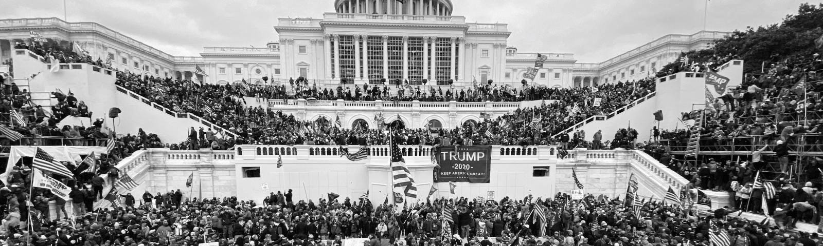 This photo shows the U.S. Capital as thousands of President Trump supporters, rioters, and insurrectionists gather to protest Biden’s election. At this point in the protest, they have breached the barriers, and are climbing over the steps. Some have made their way into the building, via breaking down doors and windows.