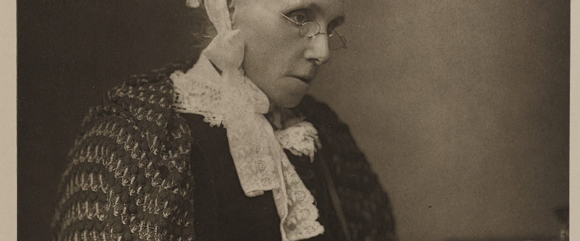 Seated monochrome portrait of novelist Isabella Banks, wearing glasses and writing on a piece of paper in her lap.