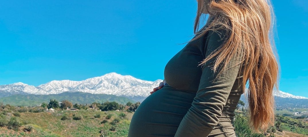 Pregnant woman in brush eyeing snow-covered mountains