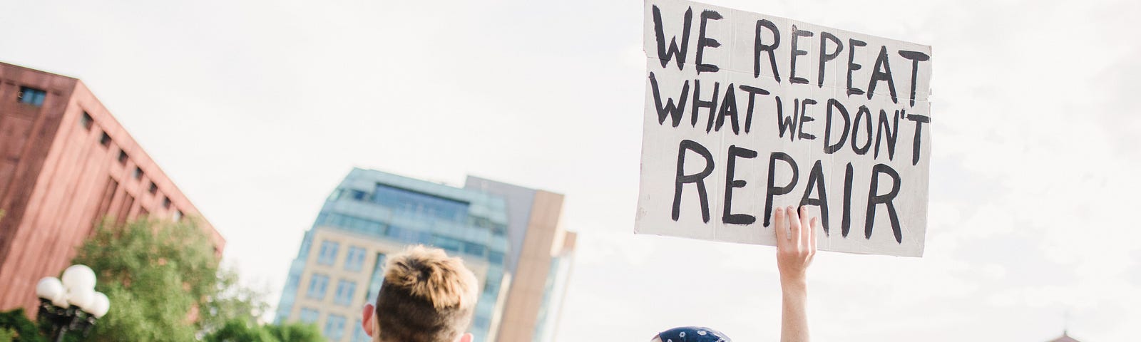 Civil Rights advocates hold a sign reading “We repeat what we don’t repair,” during a protest.