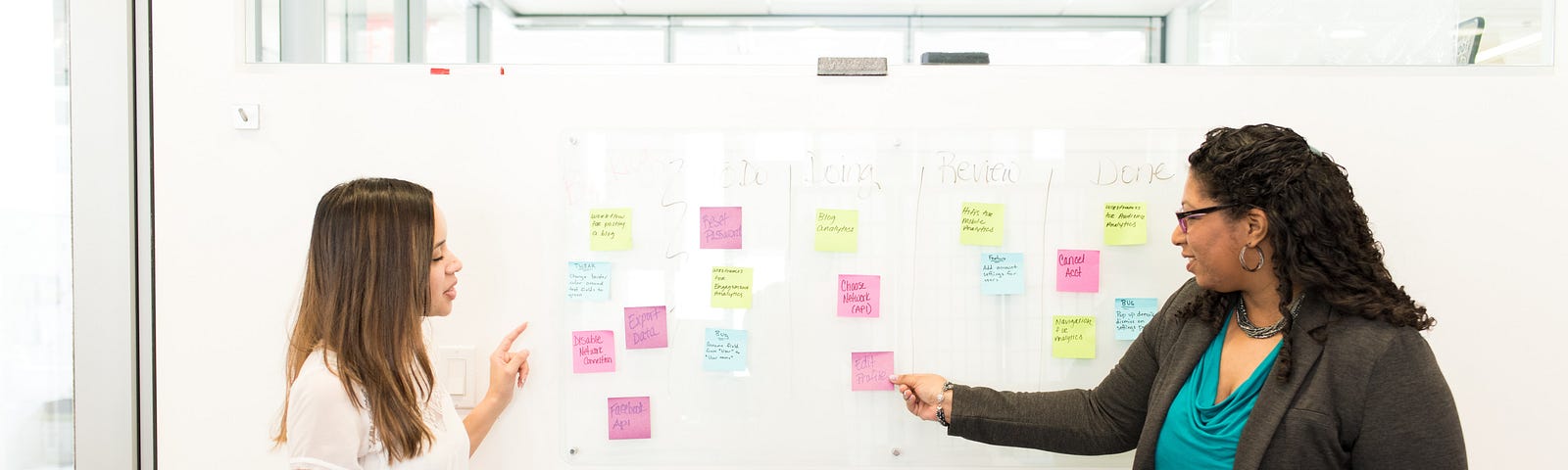 Two women using post-it notes on a whiteboard to collaborate