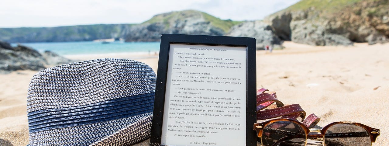 a floppy hat, an iPad displaying a story, and sunglasses on the beach. (Medium publications)