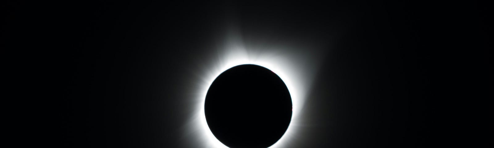 The black circle of the Moon blocking the Sun, leaving on a white halo visible on a black sky.