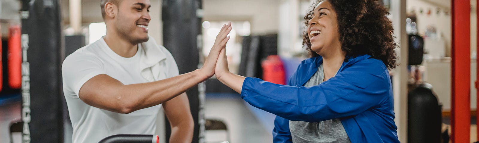 Joyful diverse trainee and fitness instructor clapping hands in gym