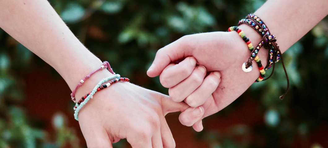 two hands with bracelets on wrists, holding pinky fingers together