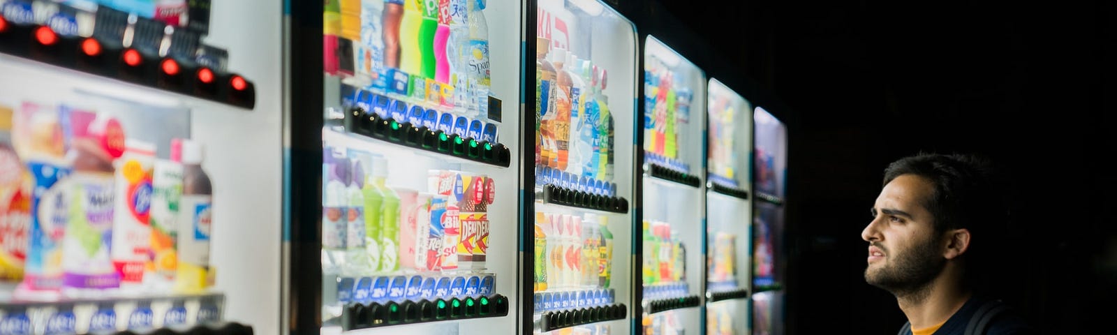 A person standing in front of glass door freezers rack filled with numerous choices of drinks.