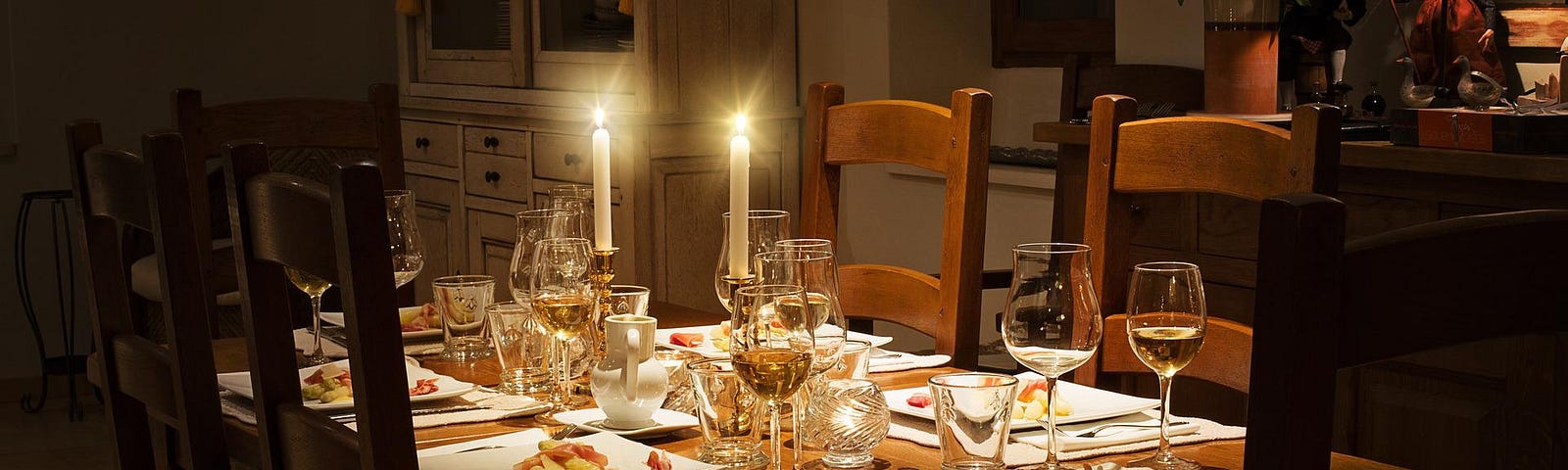 A dining room with a wooden table laid for dinner with candles and wine glasses.