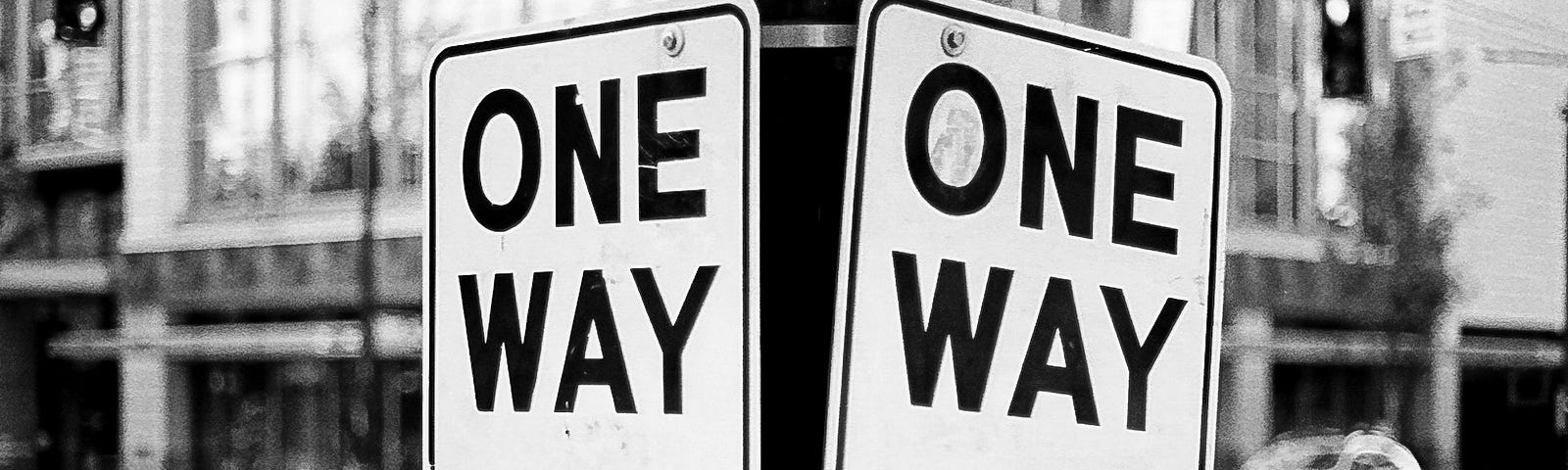 Two “One Way” traffic signs pointing in opposite directions on the corner of a city street.