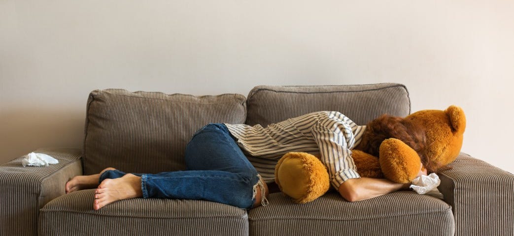 A woman cries and buries her head into a large stuffed teddy bear.