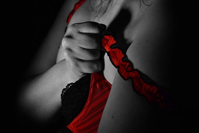 Upper torso of a woman, her hand grips the straps of a red and black corset