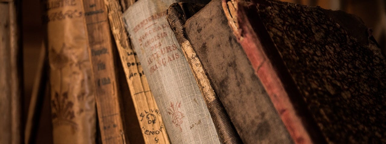 Several antique books lined up on a shelf, leaning toward the left.