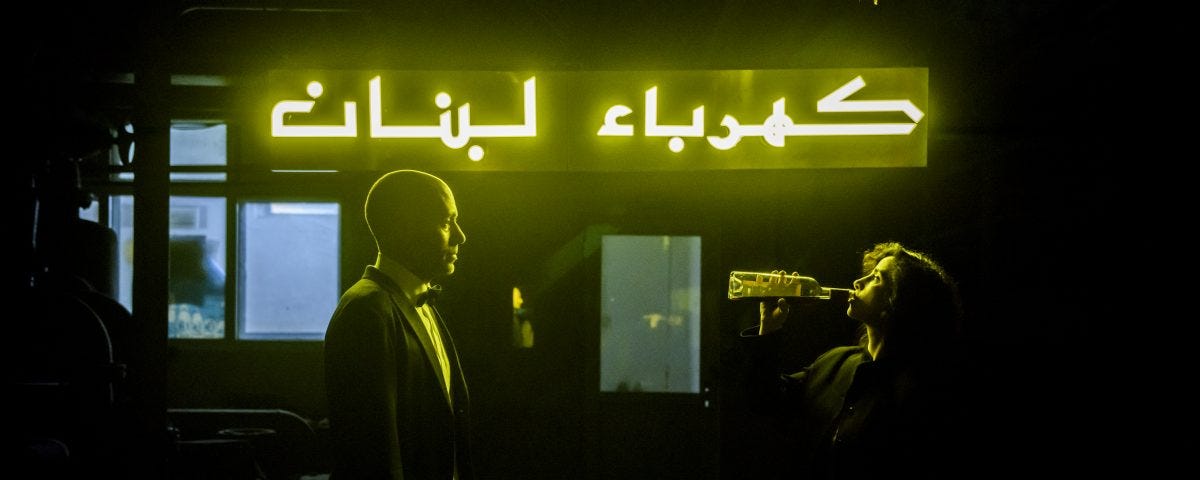 Tania and Ziad stand under the neon light of the Lebanese electricity department
