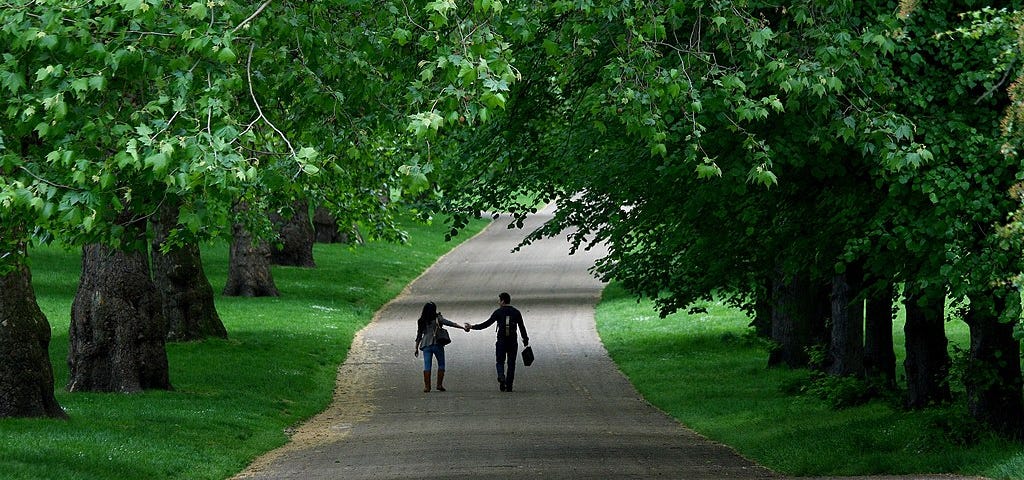 A couple touch hands as they walk through London’s Green Park.