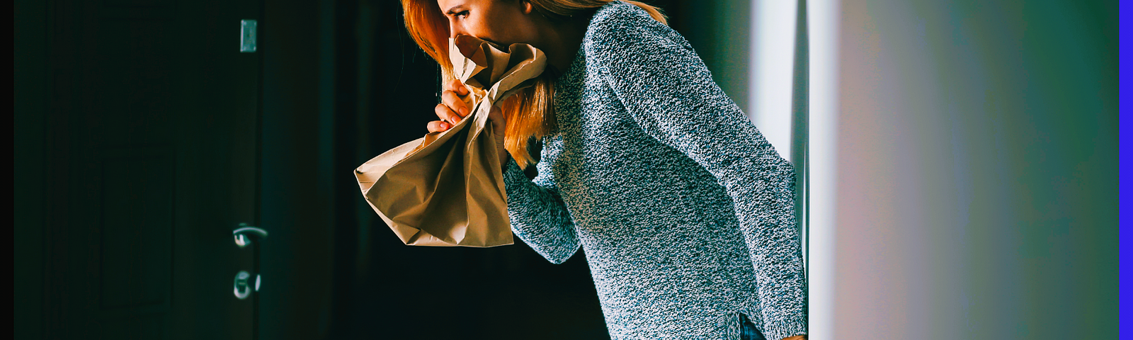 An anxiety filled woman back against the wall, blowing into a paper bag