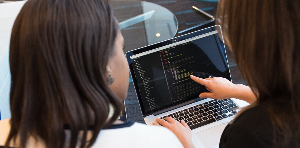 Stock image of two women looking at code on a laptop and pointing.
