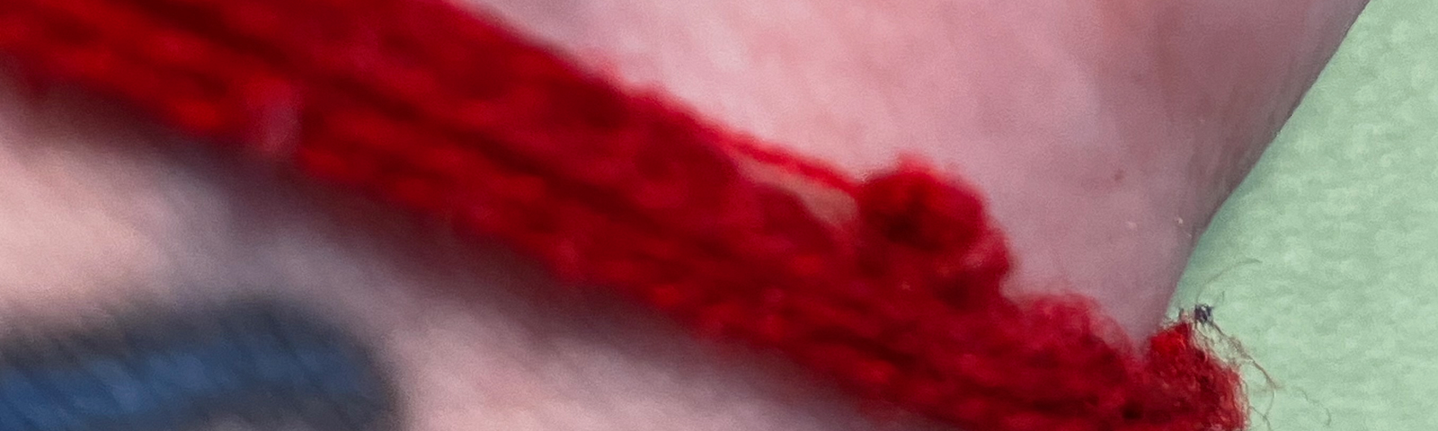 Red string with a single thread attached to the knot wrapped around the wrist of a whit person.