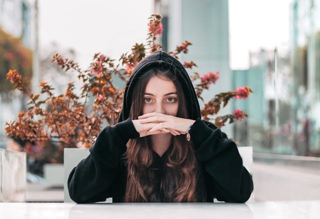 Young woman in black hoodie looking straight with a plant behind her