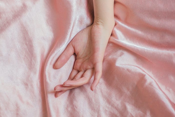A woman’s hand resting on top of pink satin sheets