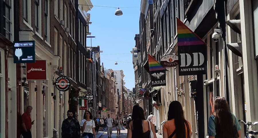 A street in Amsterdam with shops on both sides of the street and people walking by casually.