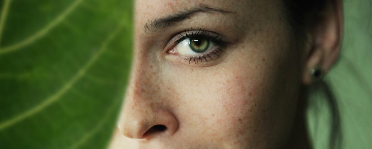 A woman’s face, half-obscured by a large green leaf.