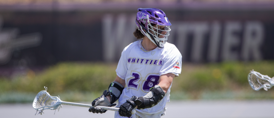 With a blurry background that reads “Whittier” om white letters, a singular player wearing a white and purple jersey. He has a purple helmet on and is holding a white racket with arm braces on. He is in motion of playing a game as he is starting to run.