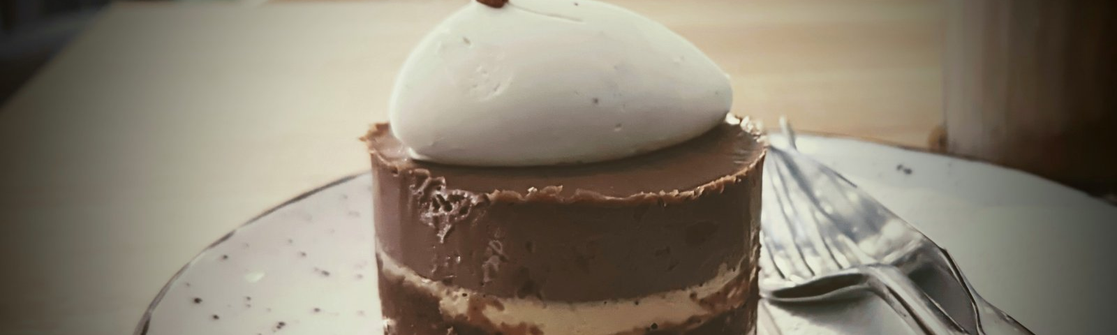 A picture of a creamy chocolate cake with cream on the top served on a plate with a fork and knife.