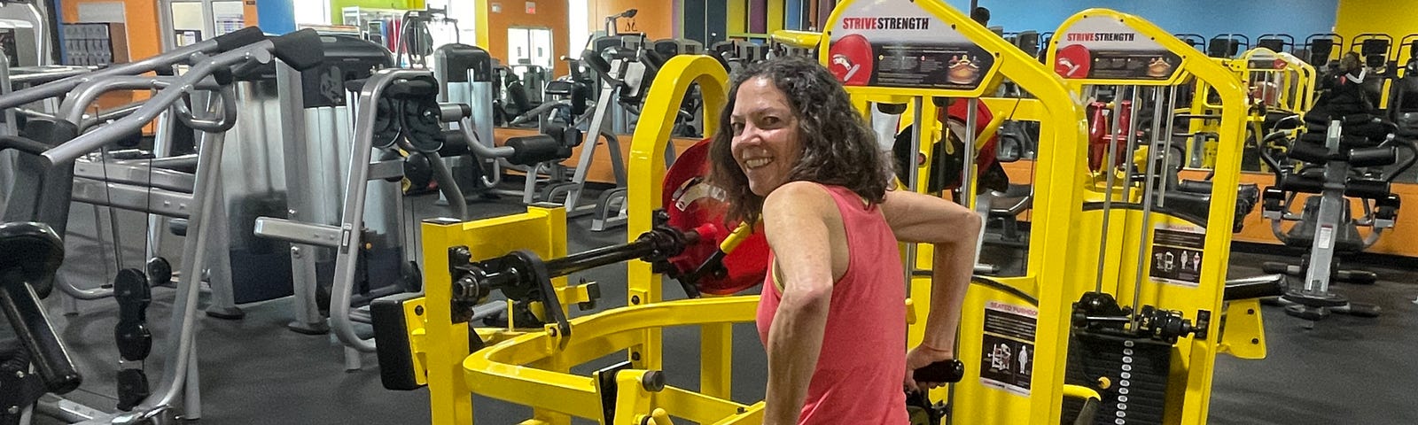 Author smiling while sitting on a weight machine, exercising at the gym.