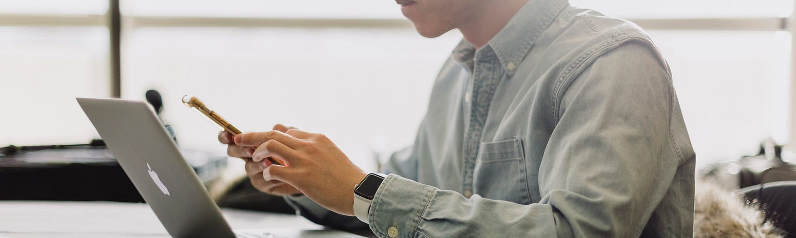 A man wearing a button-down shirt and sitting at a desk begins to make a call on his cell phone.