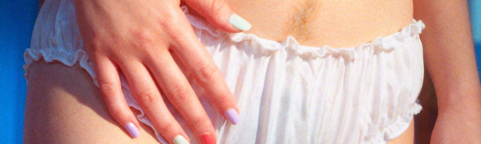 image of female lower torso wears funky multi coloured nail polish and white cotton panties