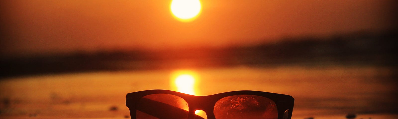 Sunglass on the beach, with the sun setting in the background