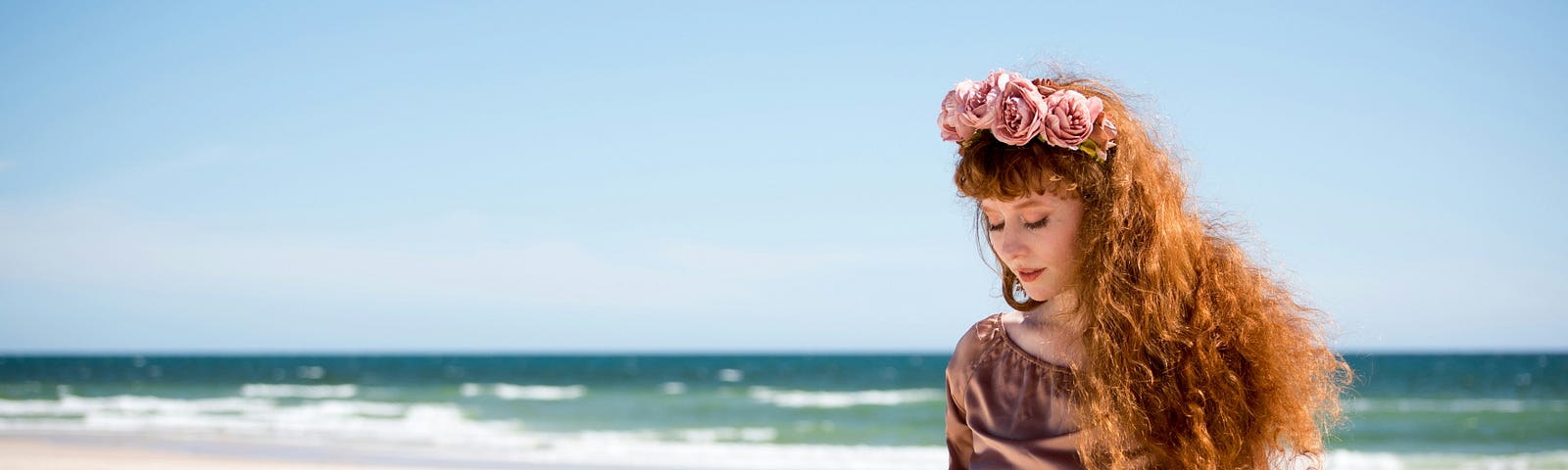 a woman with roses in her hair standing in front of an ocean on a beach