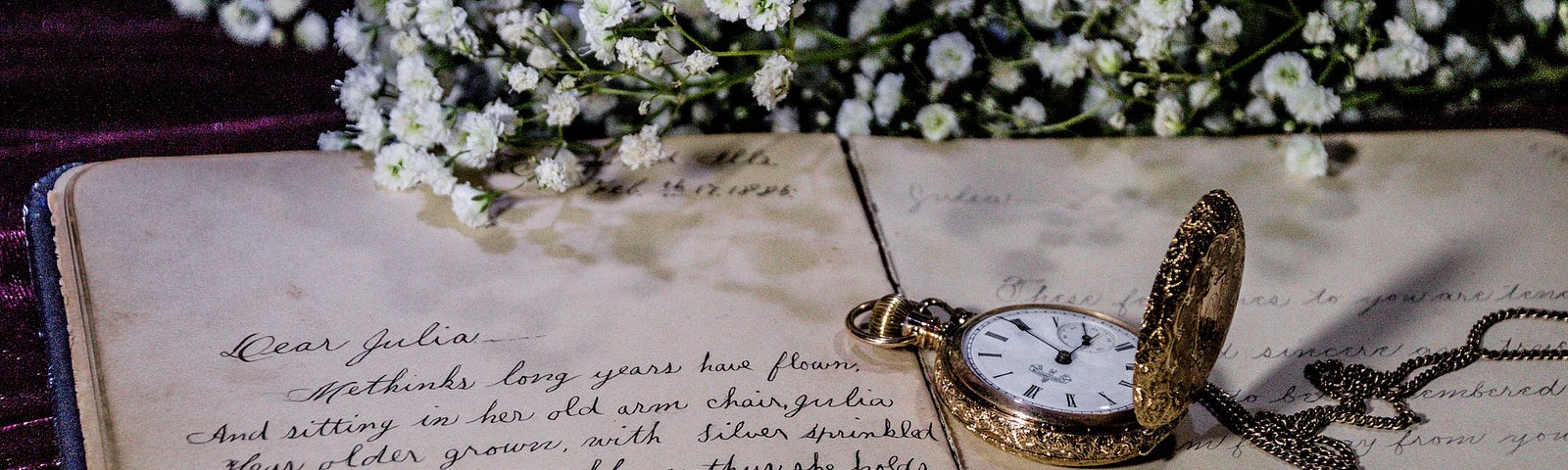 An old journal showing handwritten entry, a pocket watch and chain lies on the open pages, in the background are white flowers, baby’s breath, vintage, romantic, retro