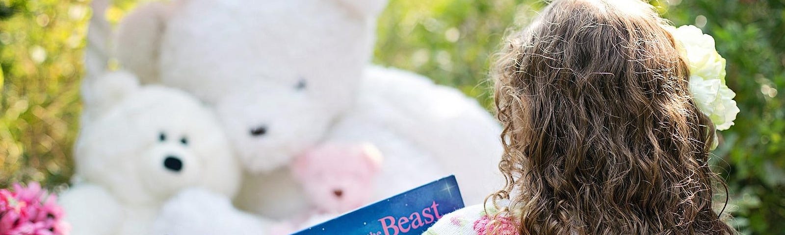 A photograph of a little girl, with her back facing so you can see her long curly locks of blond hair. She is reading a book to three stuffed fluffy bears.