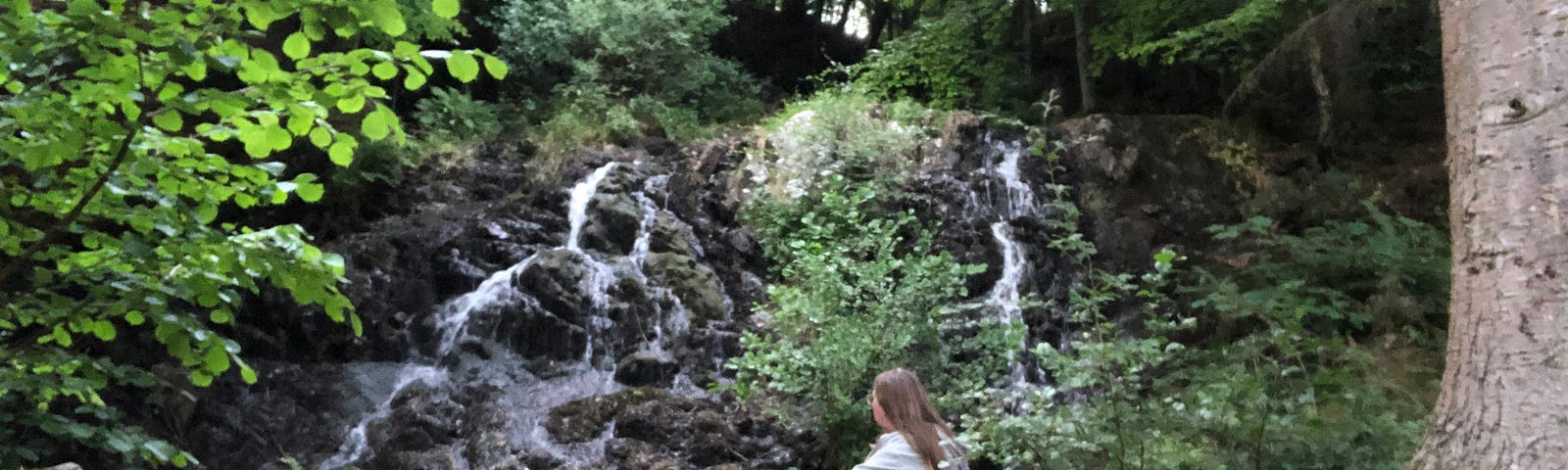 The author sitting on a rock, by a waterfall in a wood in the Scottish countryside — her natural habitat