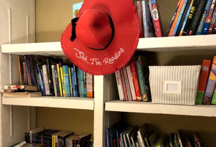 Book shelves with a large red hat in the center that reads, “Shh. . . I’m reading!”