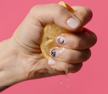 a white woman’s hand squeezing an orange slice, with juice running out between her fingers