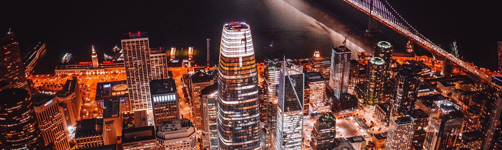 A bird’s eye view of Downtown San Francisco at night. The Salesforce tower is in the center of this evening shot with the Bay Bridge in the background.